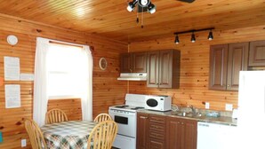 A wooden cabin interior with a dining table, chairs, a stove, microwave, cabinets, and a sink. - Mayfield Country Cottages (Mayfield)