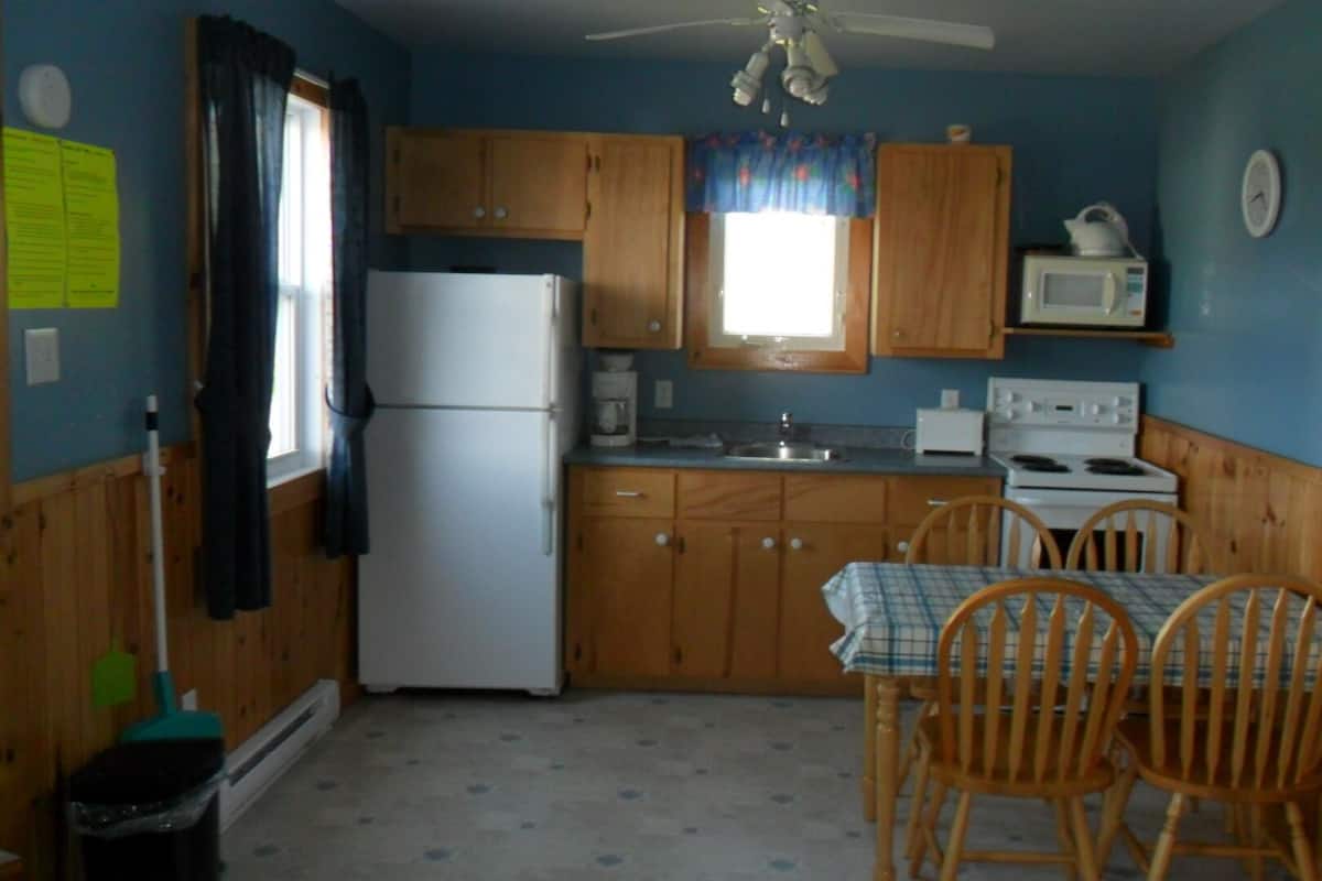 A compact kitchen with wooden cabinets, a refrigerator, a microwave, a stove, and a dining table with chairs.