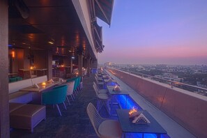 An outdoor dining area with tables and chairs, a view of the cityscape, and a sunset in the background. - Hotel Ivory Tower (Bengaluru)