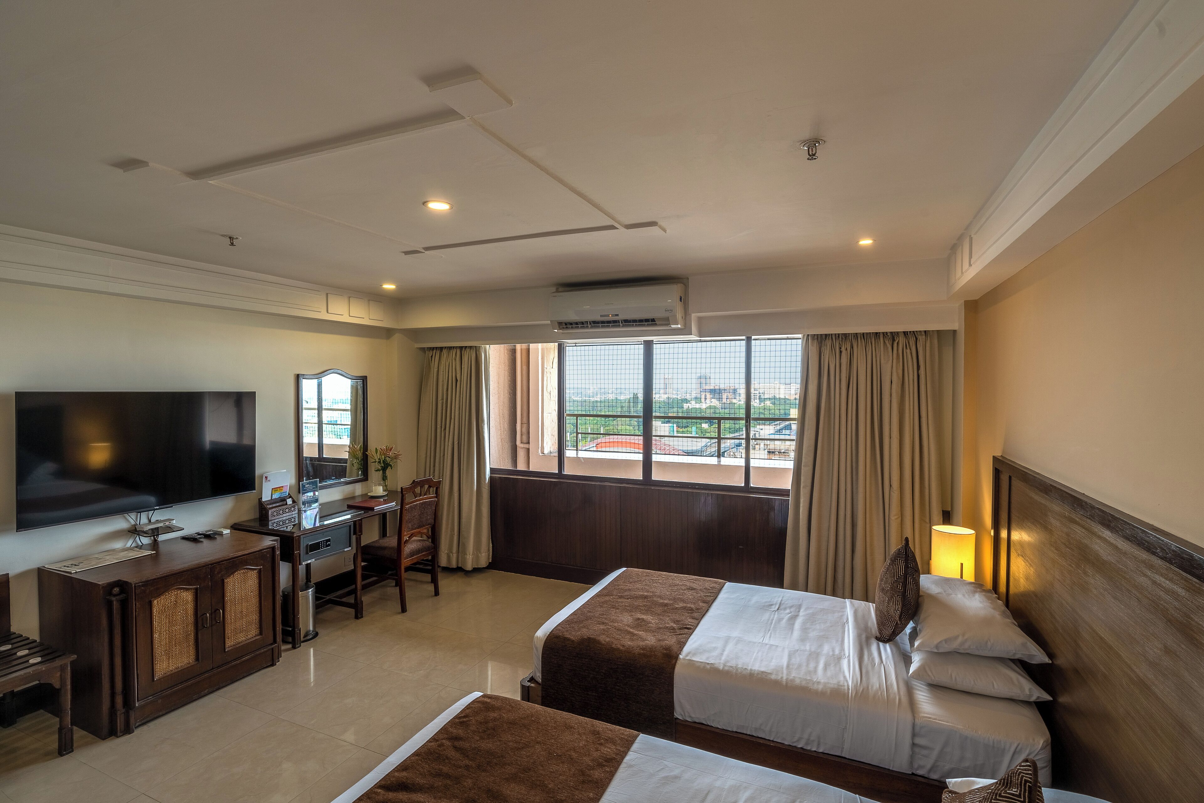 Habitación de hotel con dos camas, televisión, escritorio con silla y ventana con cortinas.