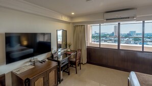 Een hotelkamer met een grote televisie, een bureau met stoel, een spiegel en een raam met uitzicht op de stad.