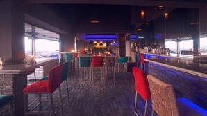 Een bar met een toonbank en krukken, grote ramen en uitzicht op de stad.