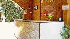 A reception desk with a telephone, a vase with flowers, and a wall with framed pictures and a calendar. - Perola Do Mar (Candolim)