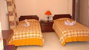 A hotel room with two beds, each with a swan-shaped towel, a nightstand with a lamp, and a wall with a floral pattern. - Perola Do Mar (Candolim)