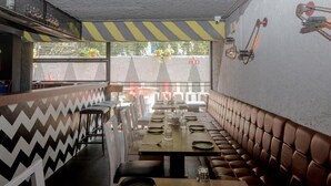 A restaurant with a long table set for dining, cushioned booths along the wall, and a view of the street outside. - Hotel Jayshree (Mumbai)