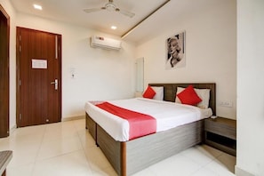 A hotel room with a bed, a nightstand, a wooden door, an air conditioning unit, and a ceiling fan.