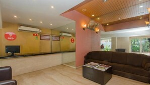 A reception area with a wooden ceiling, a brown sofa, a reception desk, and a TV screen. - Hotel Jayshree (Mumbai)