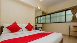 A hotel room with a bed, red pillows, a red throw, a desk, and a window with curtains. - Hotel Jayshree (Mumbai)