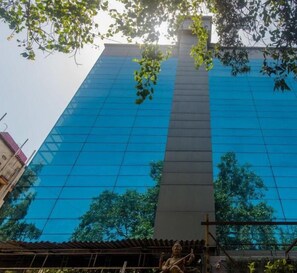 A modern building with a glass facade reflecting trees and a clear sky. - Hotel Jayshree (Mumbai)