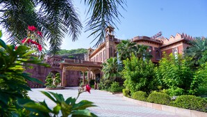 Un edificio grande e histórico con una entrada imponente, rodeado de abundante follaje y palmeras.