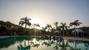 Piscina con sillones de descanso y palmeras, rodeada de edificios y estructuras cubiertas.