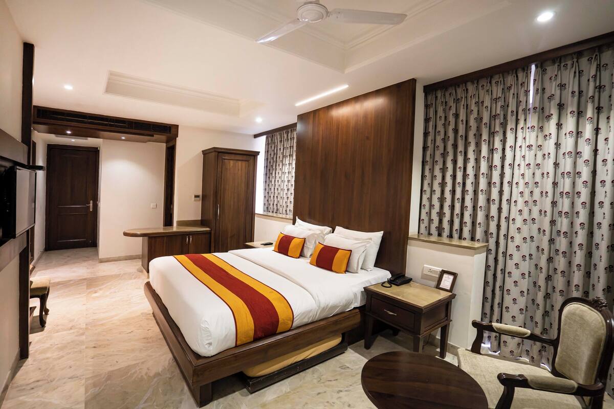 A modern hotel room with a large bed, wooden headboard, a desk, and a chair.