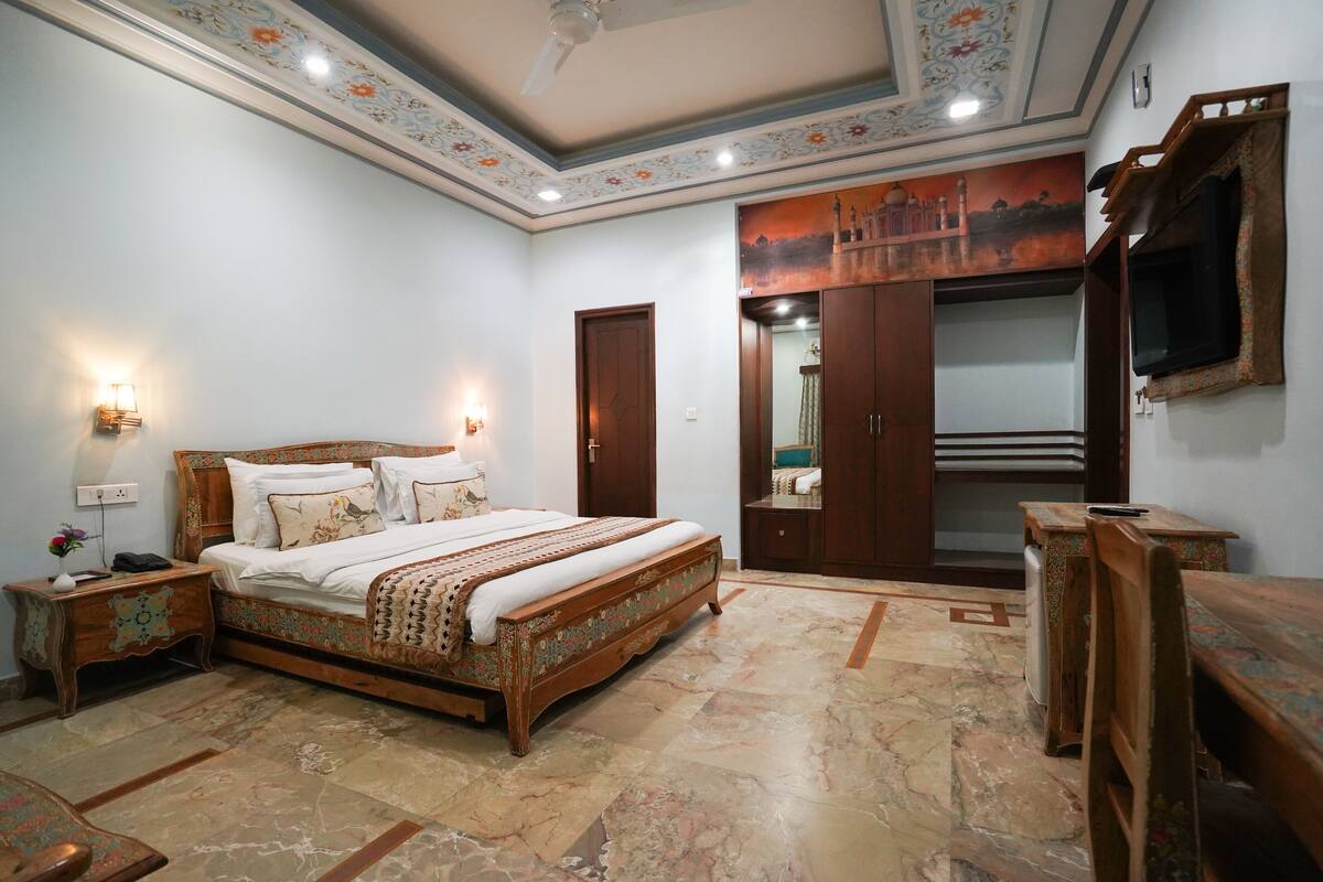A bedroom with a large bed, a wardrobe, a television, and a decorative mirror.