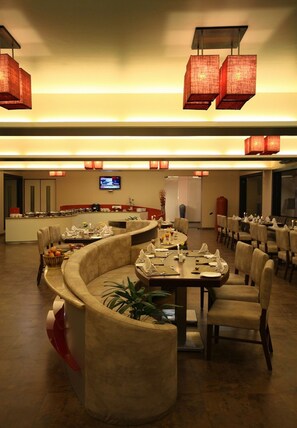 Un restaurante con un área de comedor curva, varias mesas y sillas. Hay faroles rojos colgando sobre las mesas.