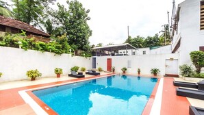 A rectangular swimming pool with a red border, surrounded by potted plants and lounge chairs. - Joys Palace (Thrissur)
