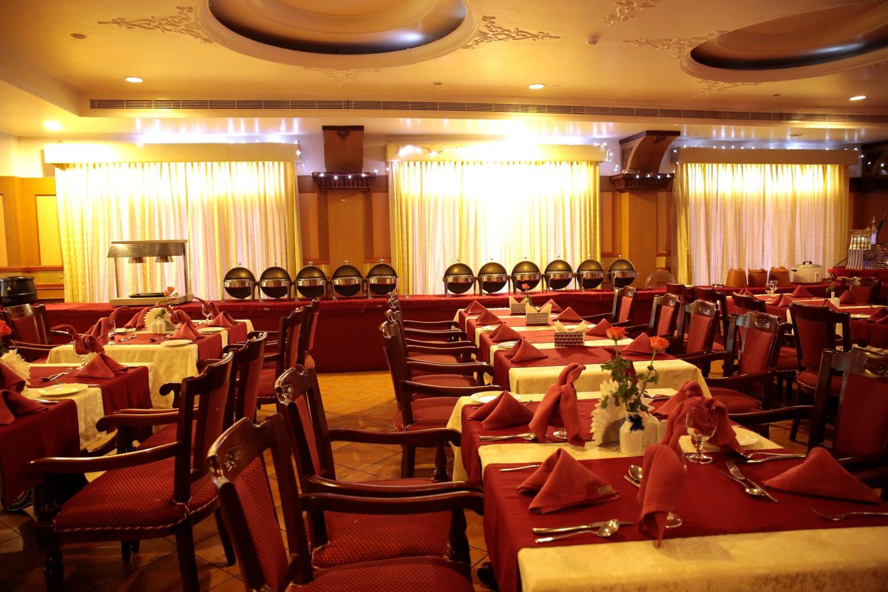 Un restaurante con varias mesas y sillas, cada conjunto con servilletas y cubiertos rojos.