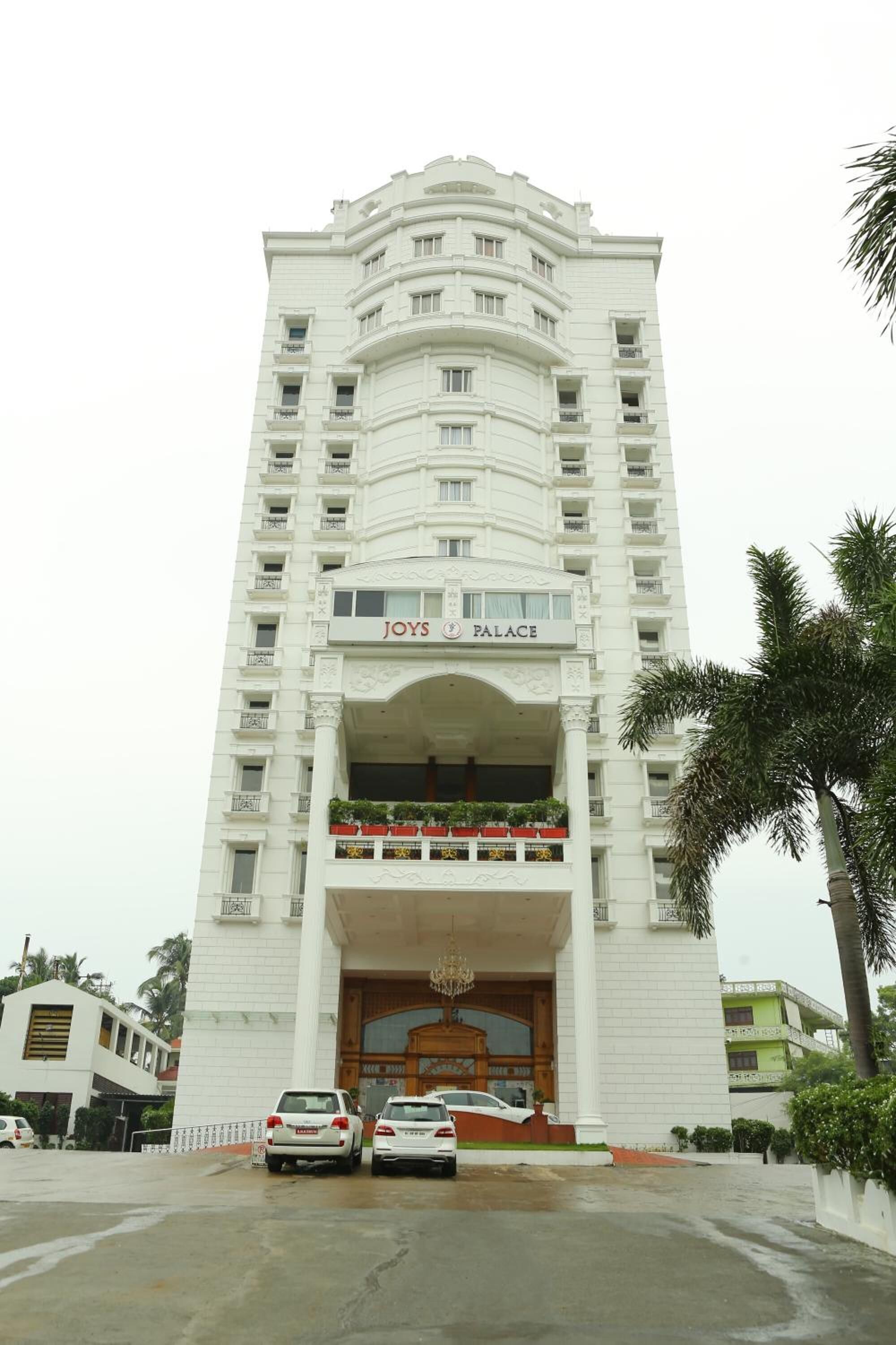 A multi-story hotel with a prominent entrance, balconies with plants, and a sign reading "Joys Palace".