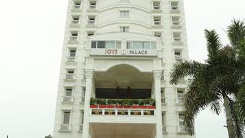A multi-story hotel with a prominent entrance, balconies with plants, and a sign reading "Joys Palace".