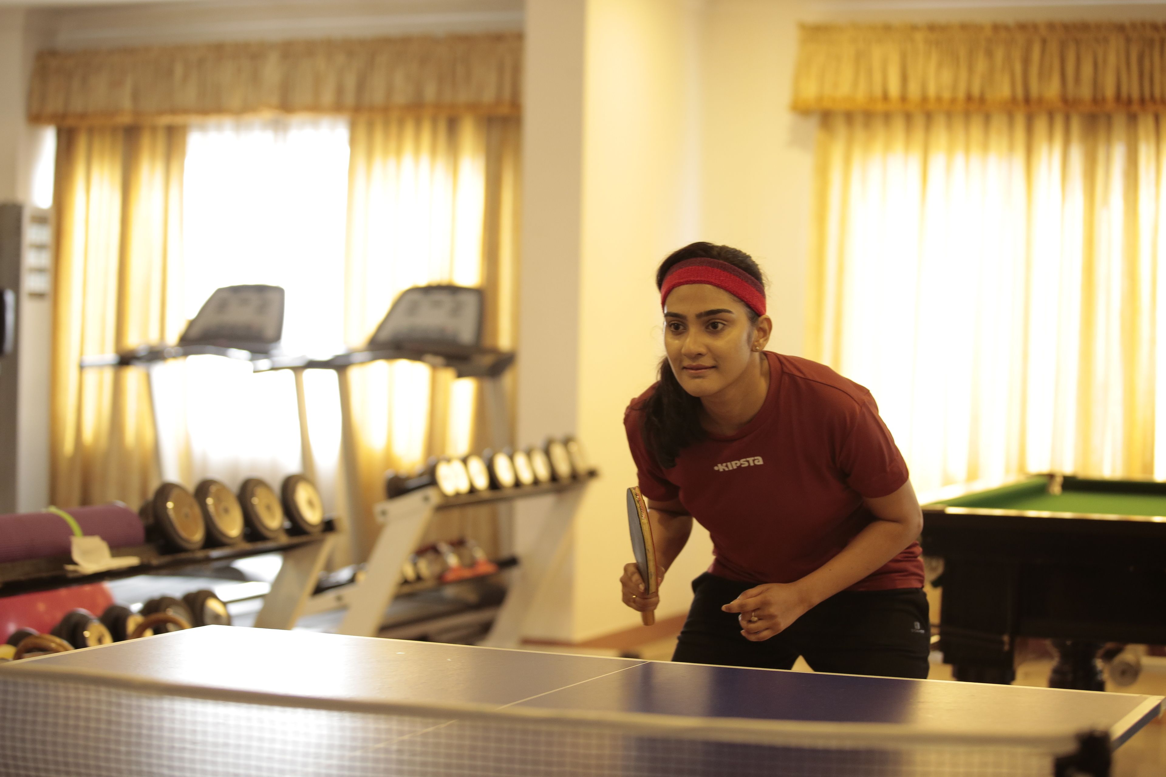 Una persona jugando ping-pong en una sala con mesa de billar, equipo de ejercicio y mesa de carambola.