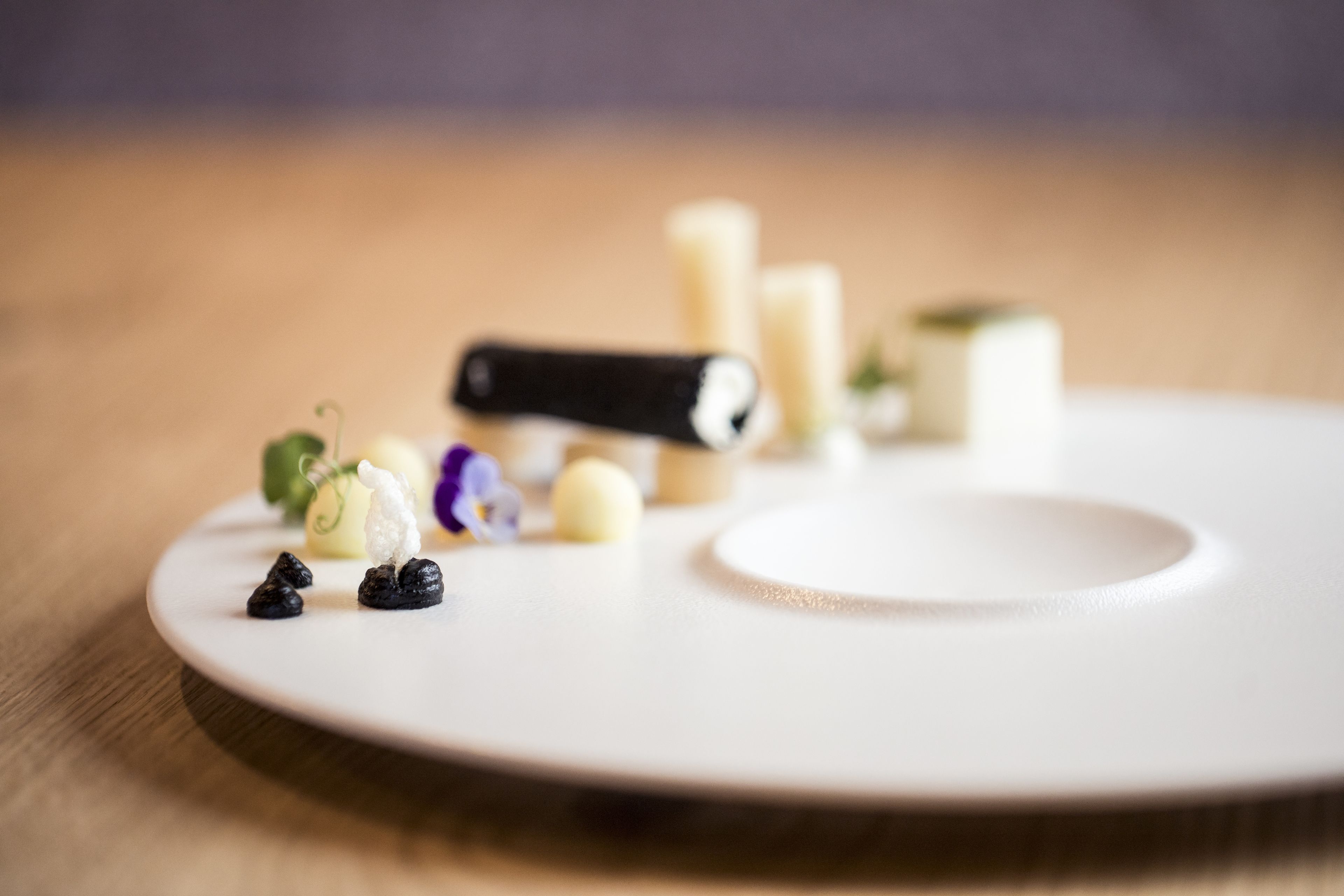 A white plate with various food items and a black object on a wooden surface.