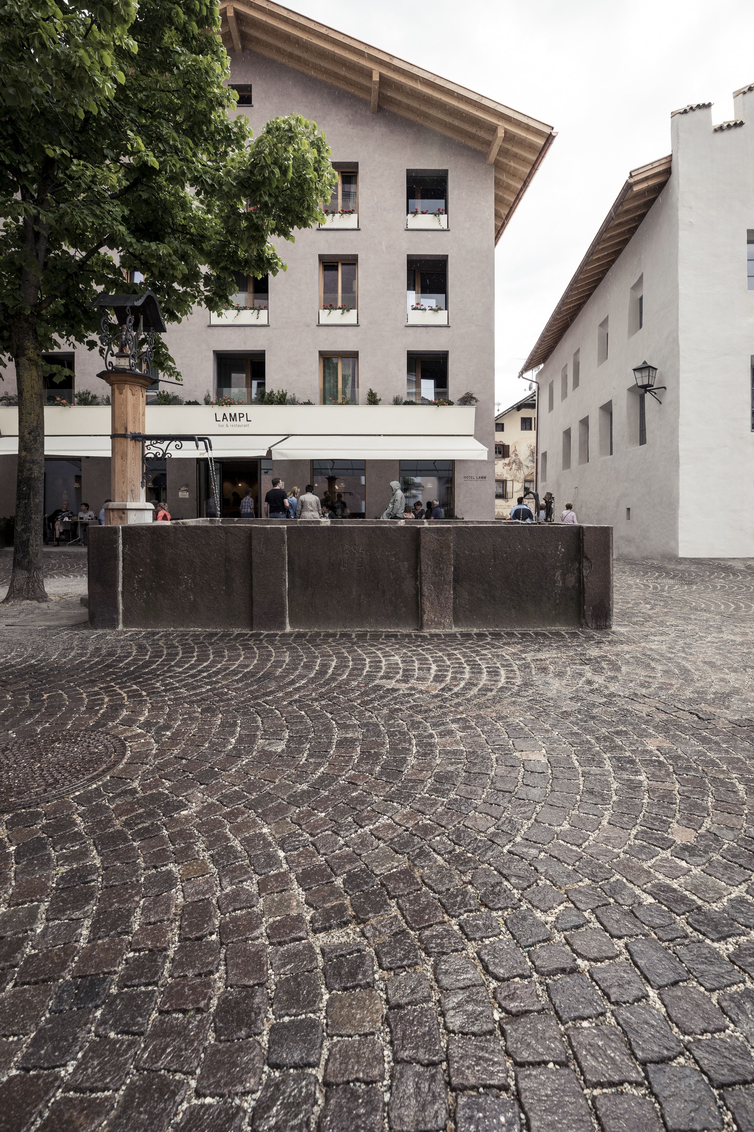 Una plaza adoquinada con un edificio que tiene la leyenda 'LAMPL' al fondo.