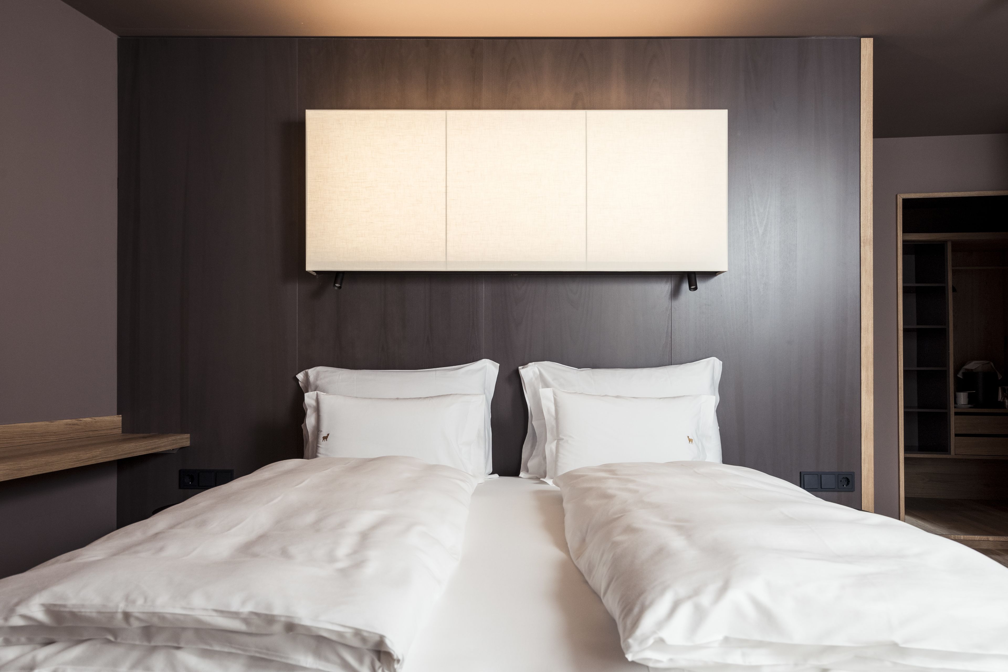 Una habitación de hotel moderna con una cama grande, un cabecero de madera y una estantería empotrada.