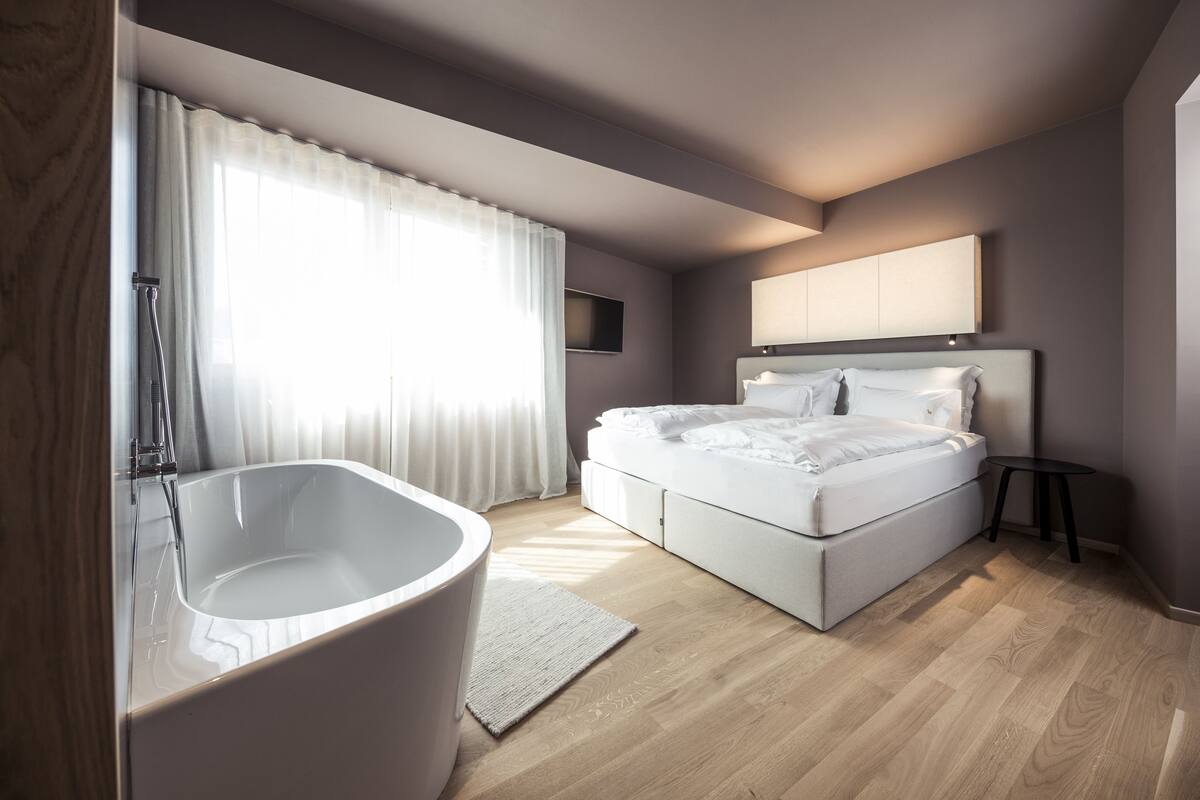 A modern bedroom with a large bed, a built-in bathtub, and a flat-screen TV.