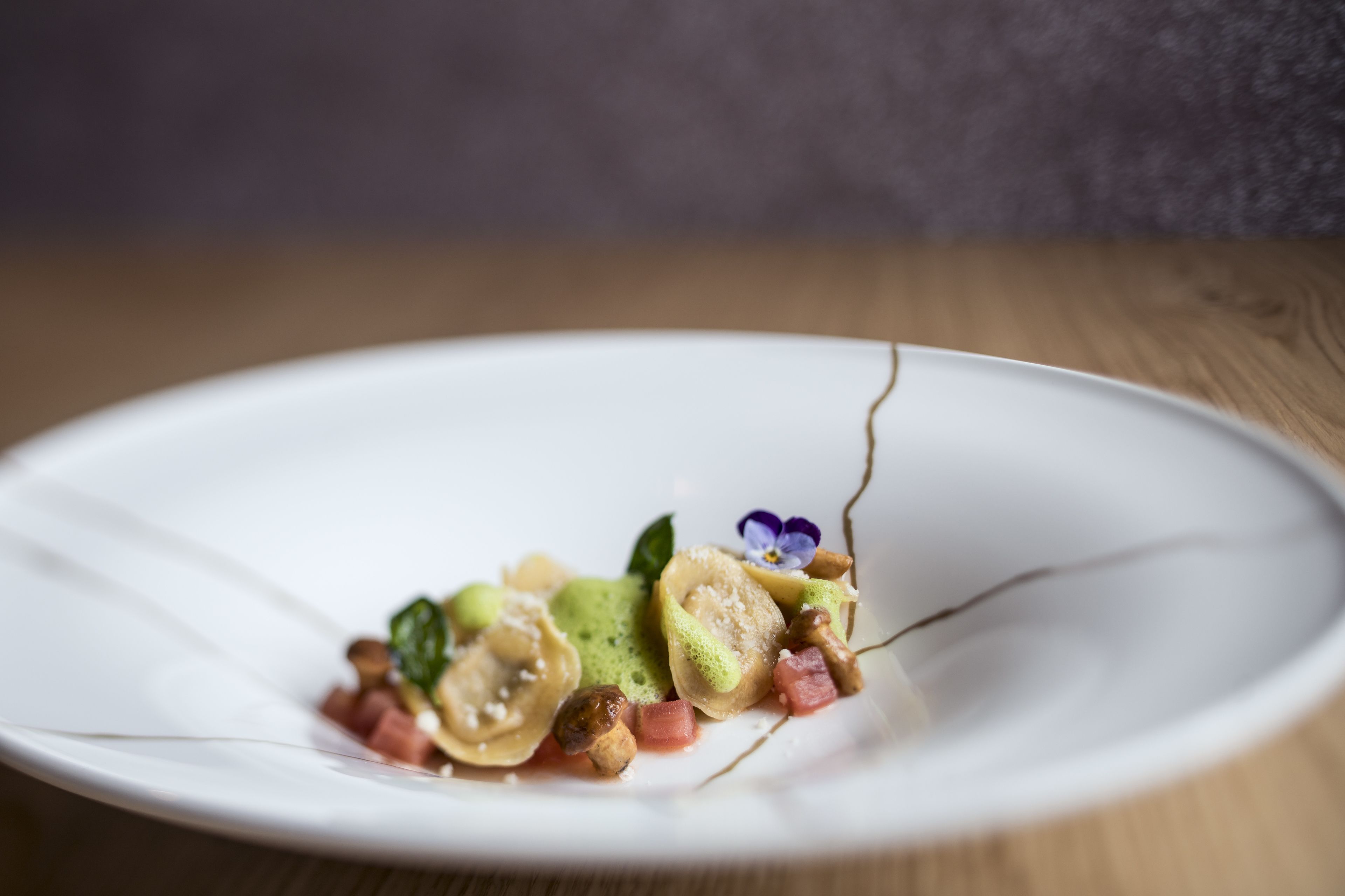 Un plato blanco con diversos alimentos, incluyendo dumplings, verduras y una pequeña flor.