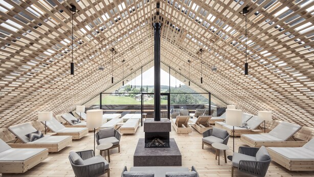 Amplia sala de estar con diversas opciones de asientos, una chimenea central y ventanas grandes con vistas al exterior.
