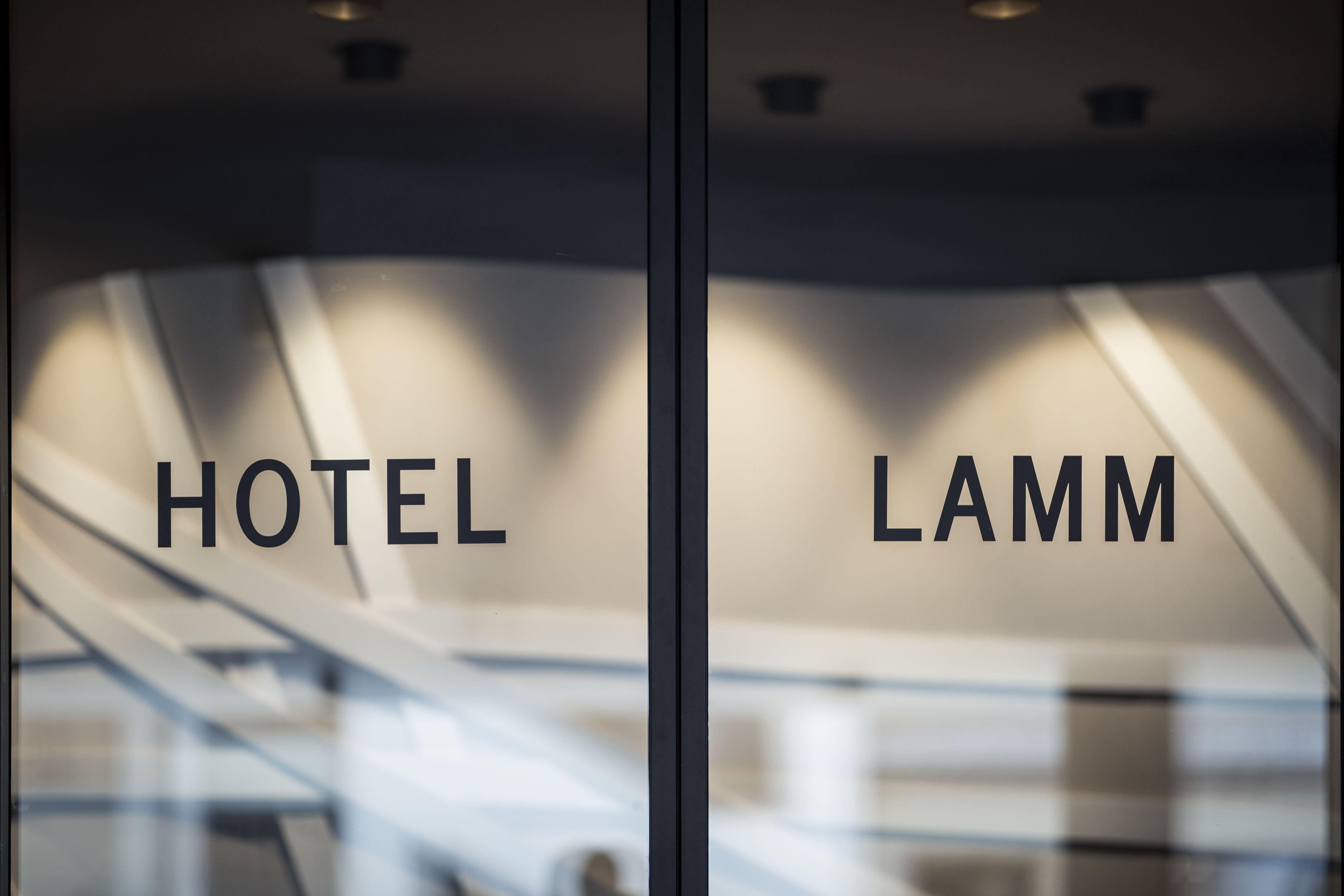 A hotel interior with a modern design, featuring a glass wall with the words "HOTEL" and "LAMM" visible.