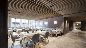 A spacious dining area with multiple tables and chairs, a modern ceiling design, and large windows providing natural light. - Hotel Lamm (Castelrotto)