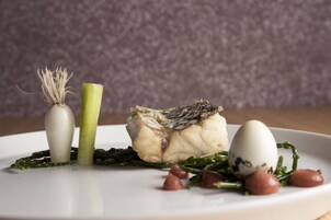 A plate of food with a boiled egg, a piece of fish, and some greens.