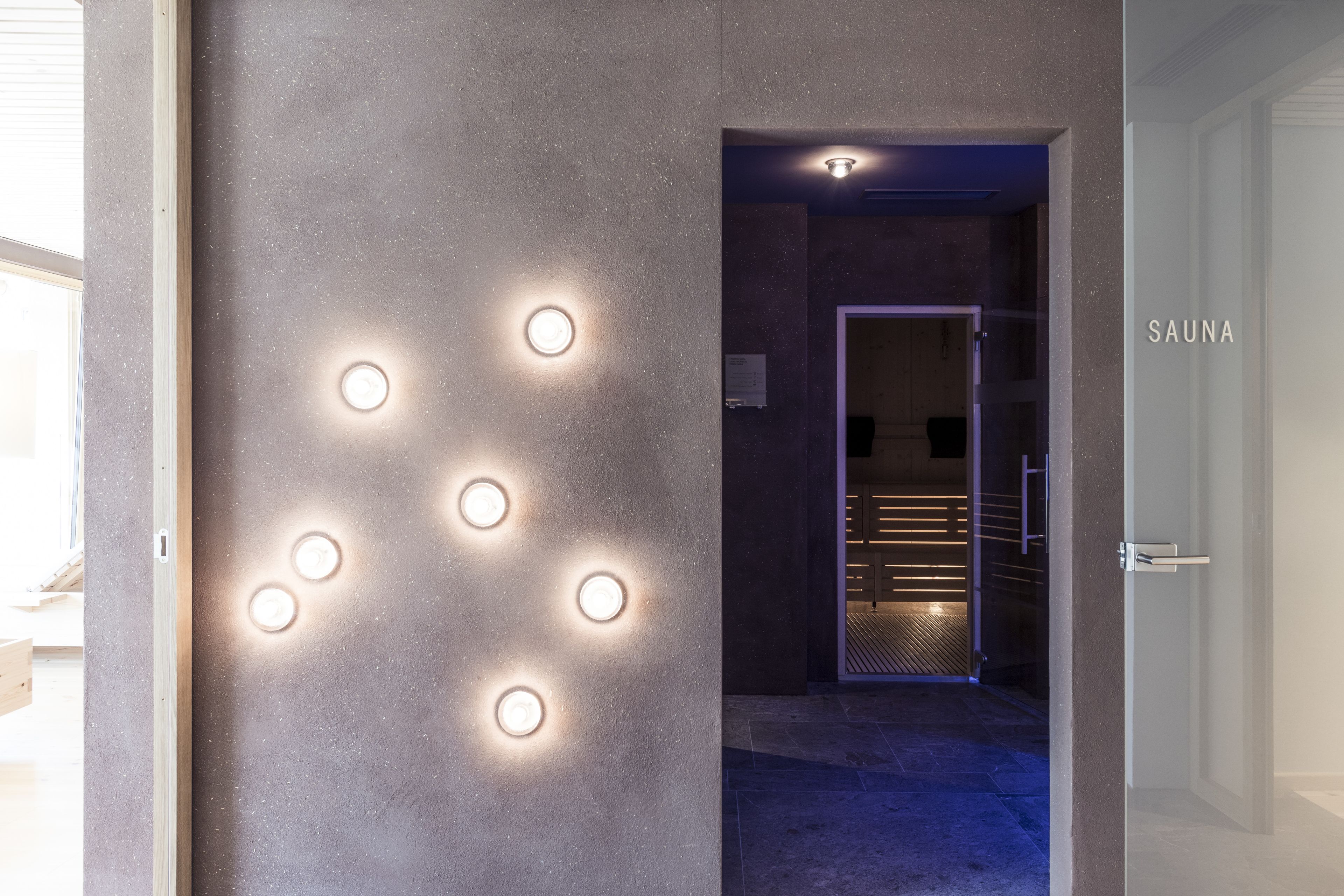 A hallway with a wall featuring circular lights and a sign labeled "SAUNA".