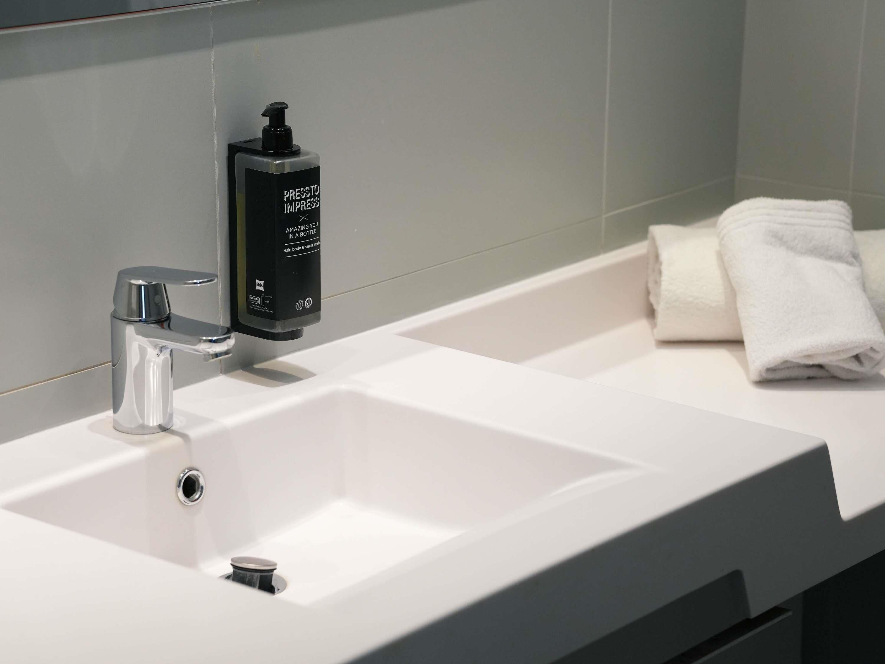 A modern bathroom with a chrome faucet, a bottle of hair and body wash, and neatly folded towels.