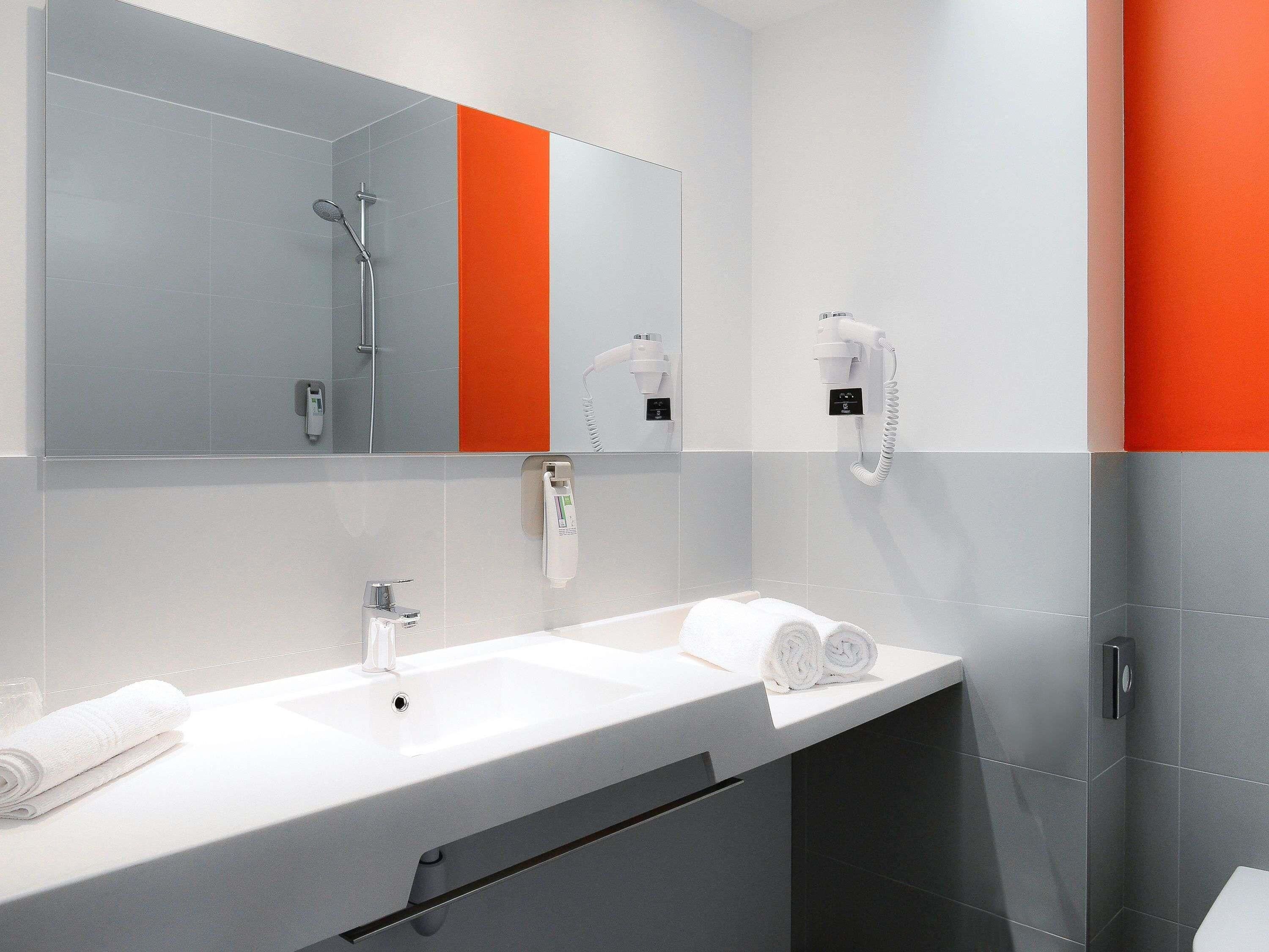 Un baño moderno con un espejo grande, dos lavamanos, una ducha y un secador de pelo.