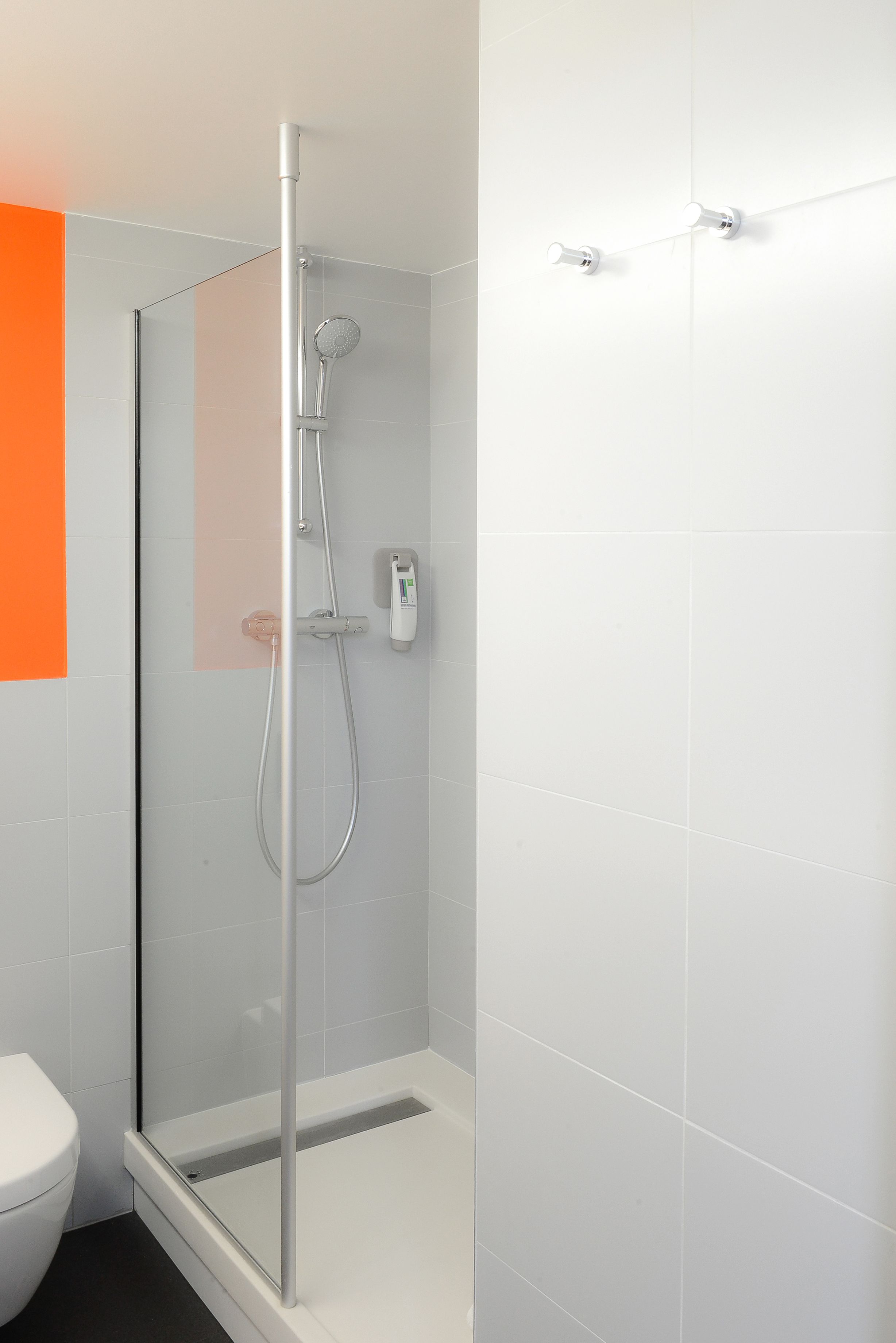 A modern bathroom with a glass-enclosed shower, white tiles, and a visible toilet.