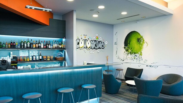 Zona de bar moderna con una barra azul, taburetes y una pared con un vibrante mural verde.