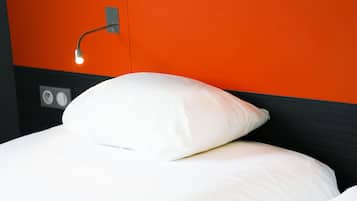 A bed with white bedding and a white pillow, a wall socket, and a light fixture.