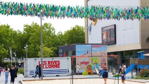 Una zona de playa con cancha de voleibol de arena, un edificio grande con un cartel que dice 'plage' y un camión 'LES RIVES DE L'ORNE' estacionado cerca.