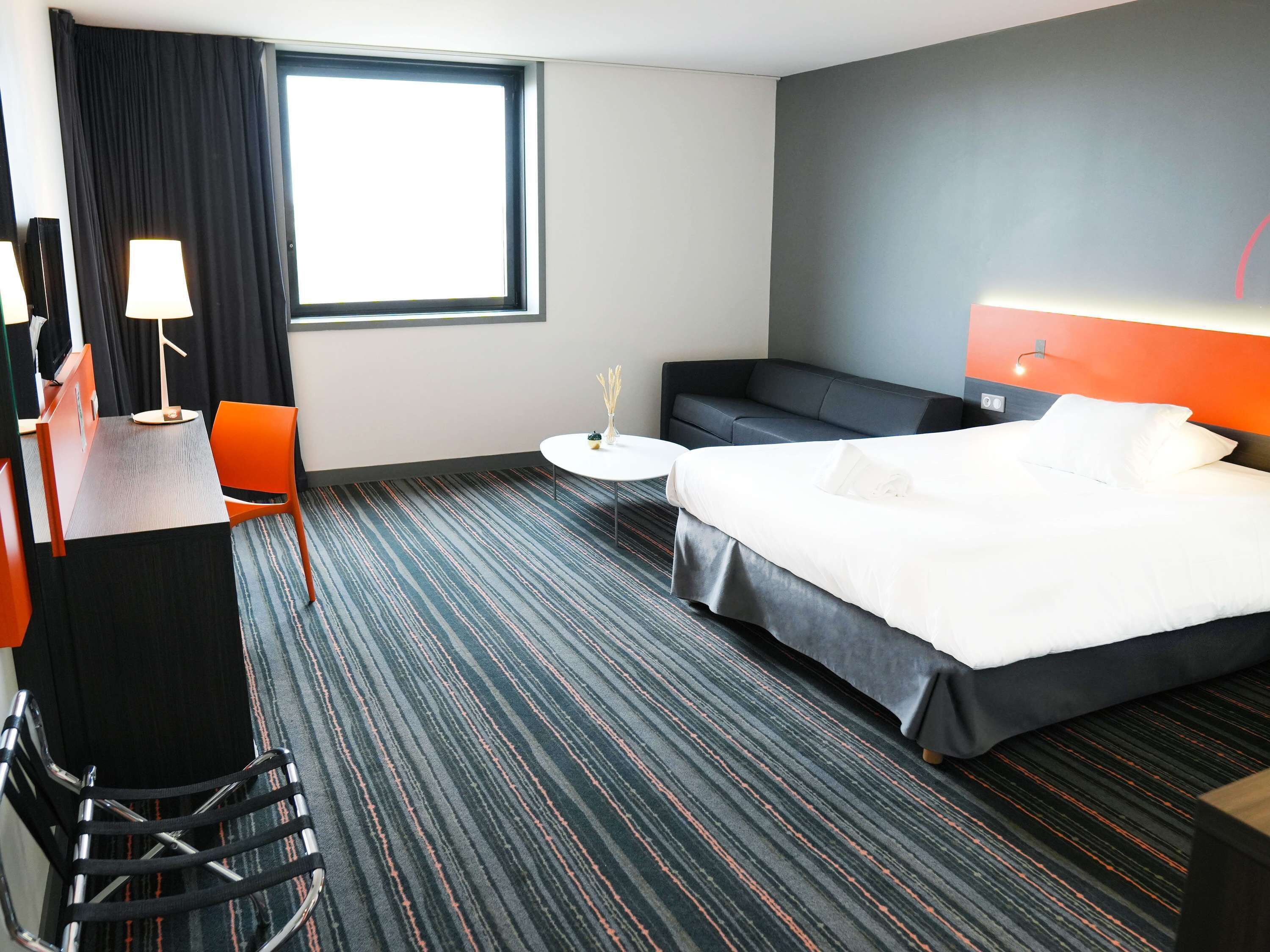 Een hotelkamer met een bed, een bureau met lamp, een stoel, een bank en een kleine tafel.