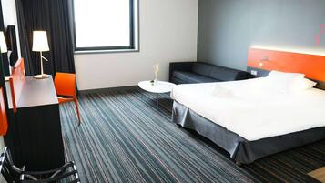 Een hotelkamer met een bed, een bureau met lamp, een stoel, een bank en een kleine tafel.