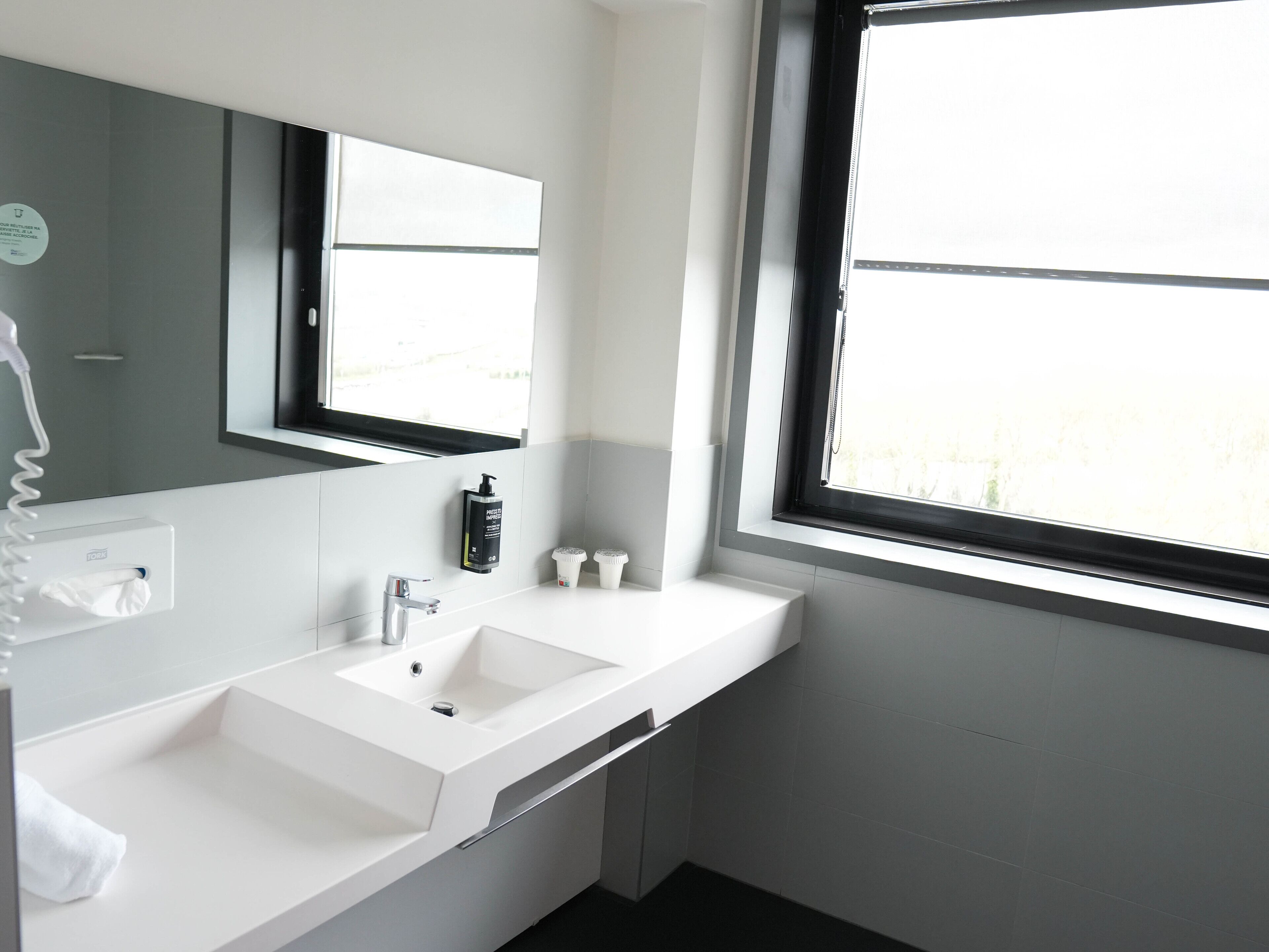A modern bathroom with a white sink, a mirror, and a window.