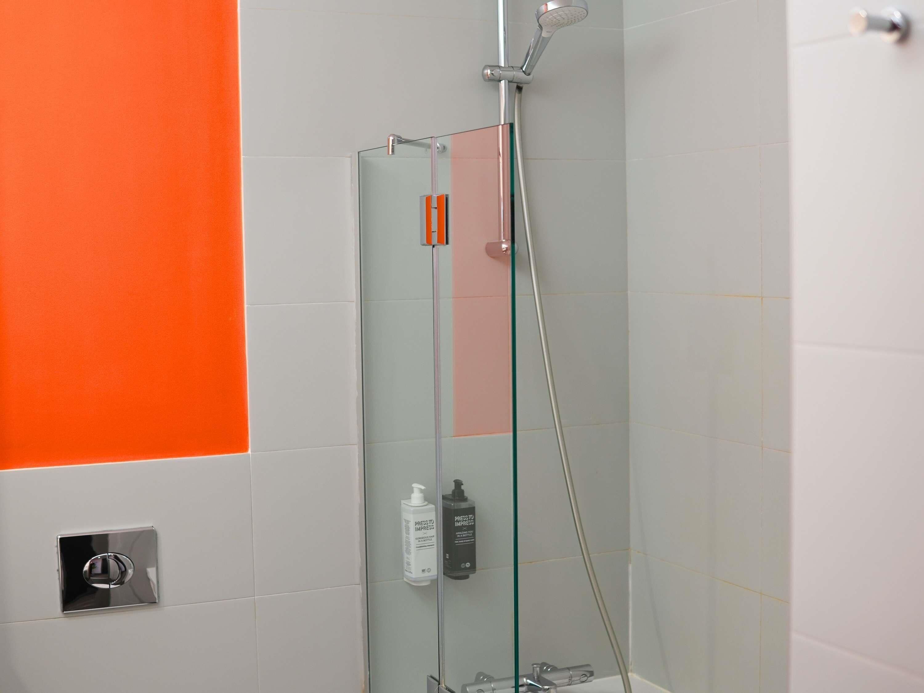 En dusch med glasväggar, ett handhållet duschmunstycke, en kontrollpanel och två flaskor schampo och balsam.