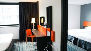 A hotel room with two beds, a desk, a chair, a lamp, and a large mirror.