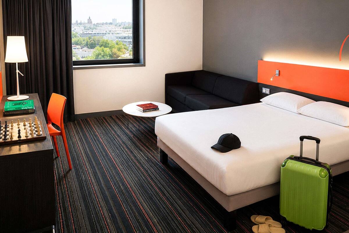Een hotelkamer met een bed, een bureau met lamp, een stoel, een kleine tafel, een bank en uitzicht op de stad.