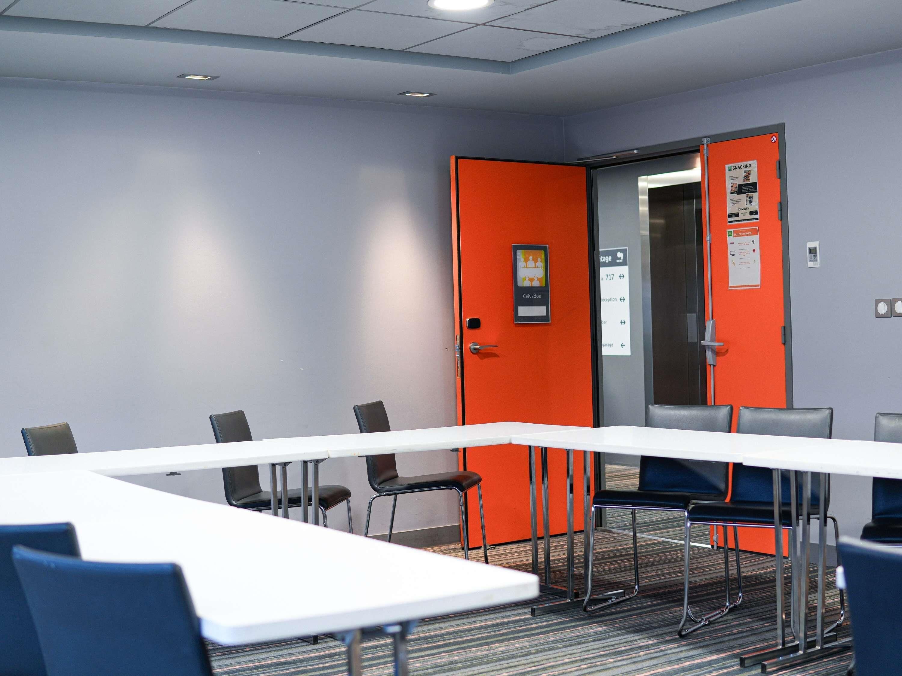 A conference room with a long table, chairs, an orange door, and a sign indicating a smoking area.