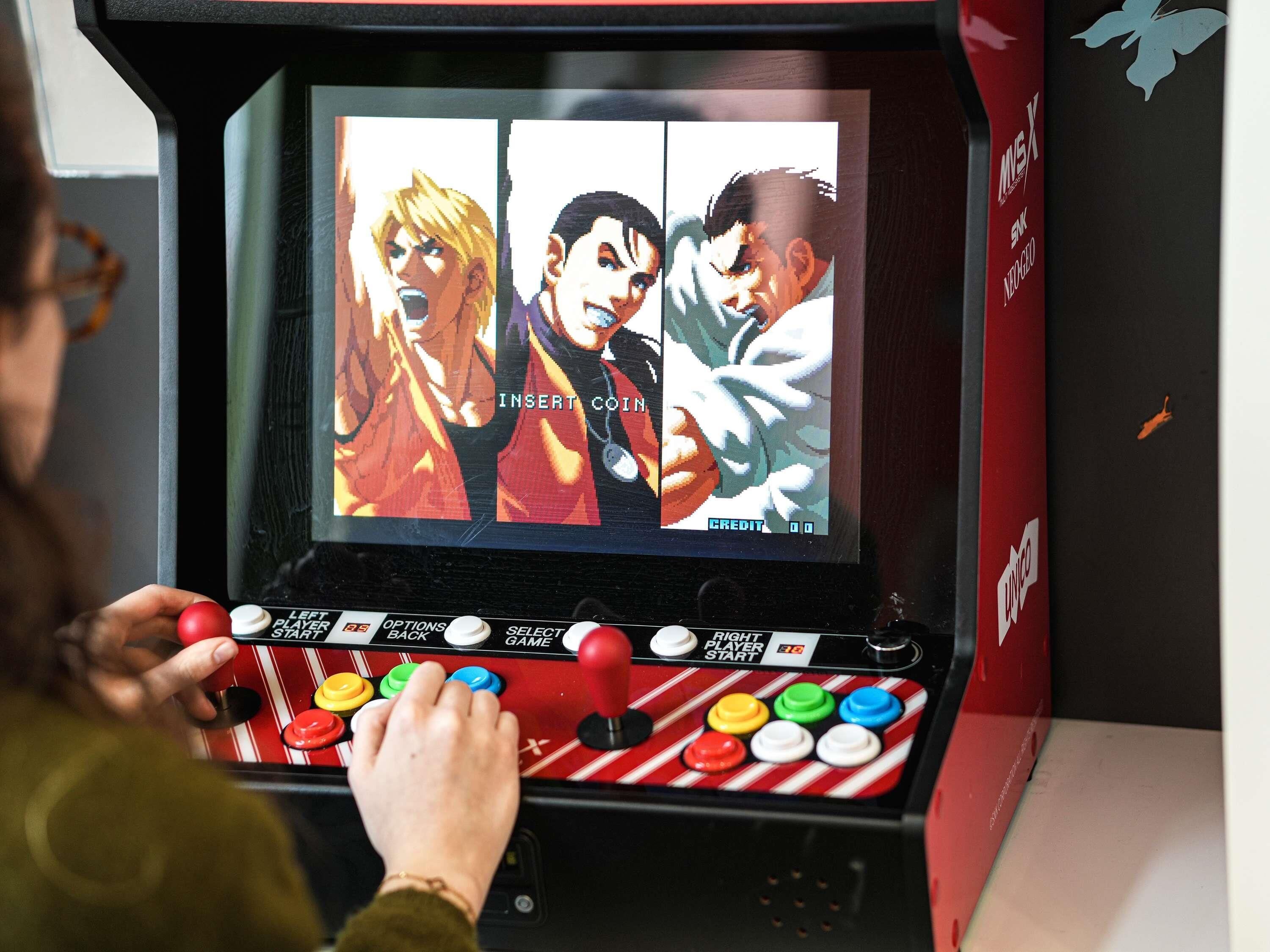A person playing a video game on a console with colorful buttons and a screen displaying anime characters.