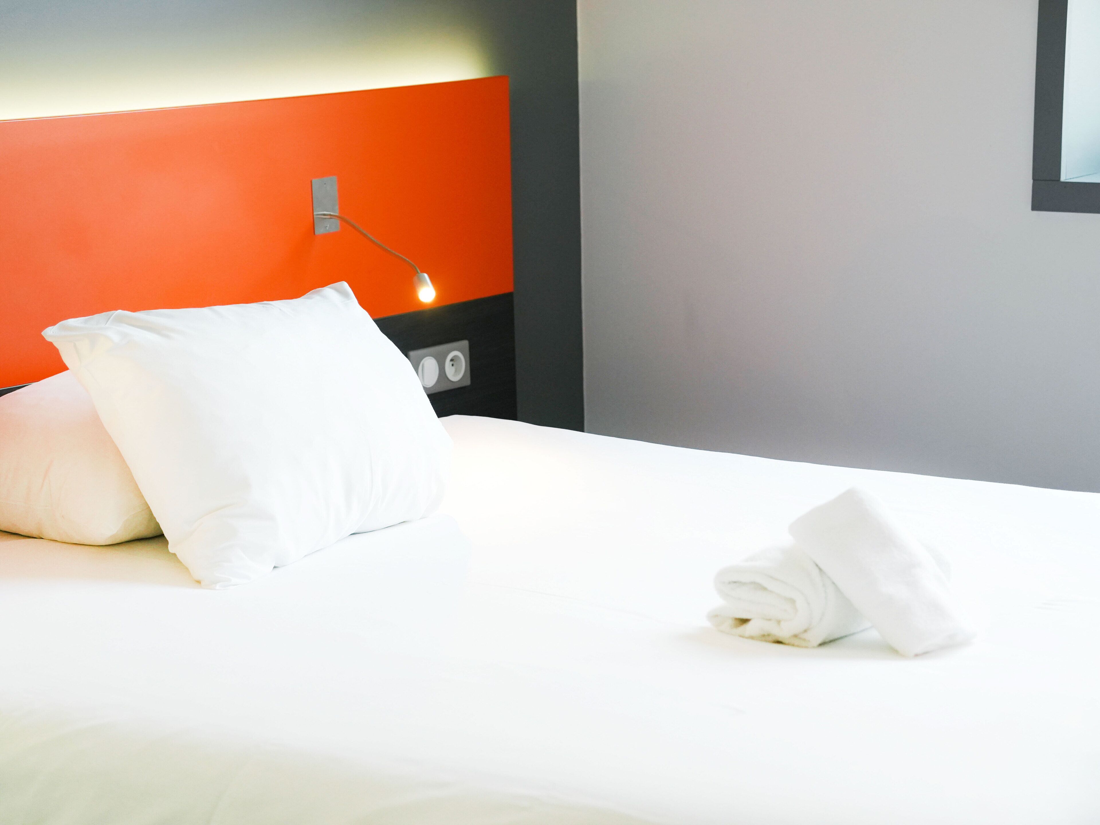 Un lit bien fait, avec des draps blancs, un oreiller blanc et une serviette pliée posée sur le côté.