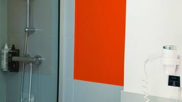 A bathroom with a shower, a white and orange wall, and a hairdryer on a white stand.