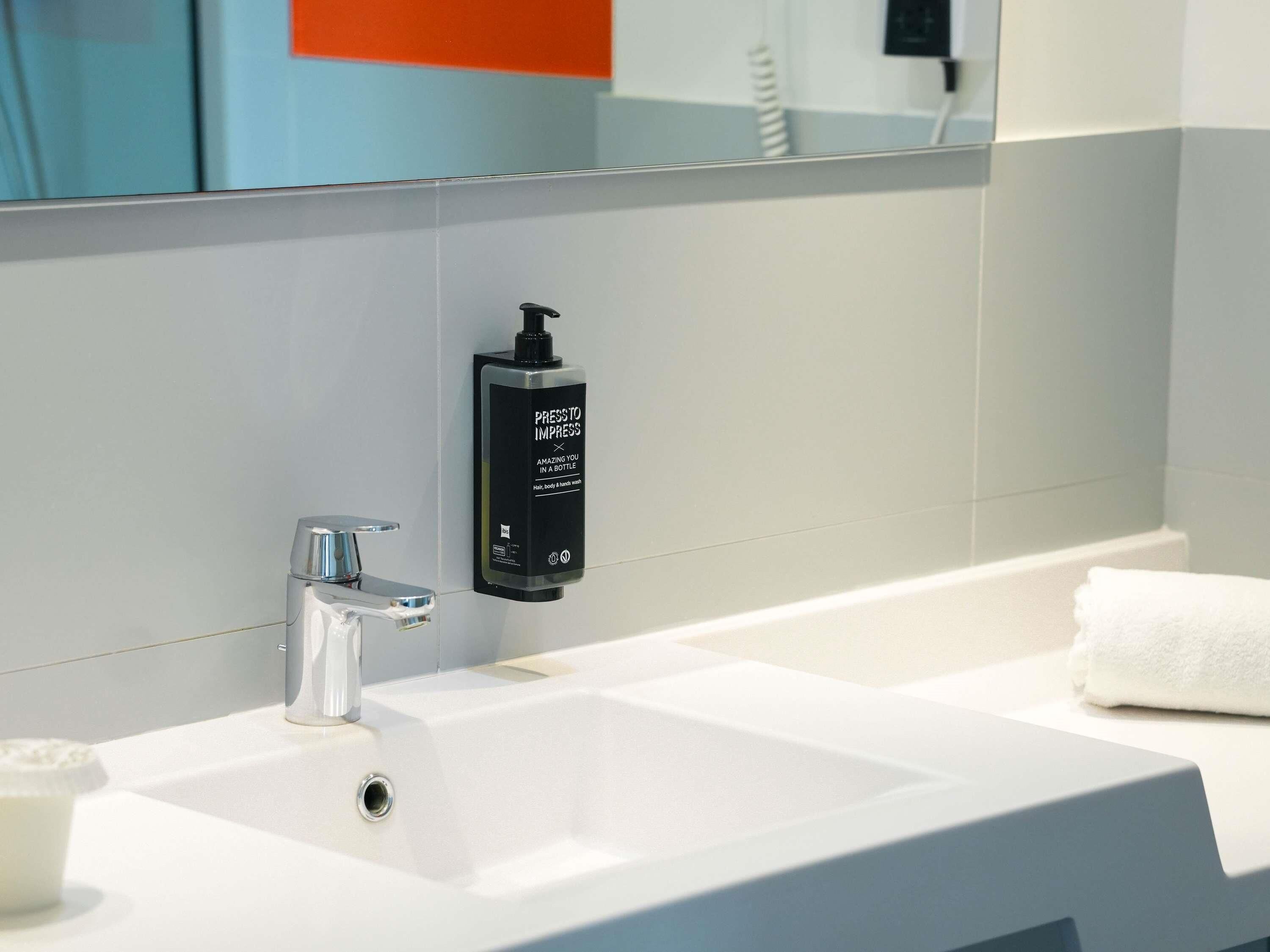Une salle de bain moderne avec un lavabo blanc, un robinet chromé et un distributeur noir sur lequel est inscrit : « APPUYEZ POUR ÉBLOUIR ».